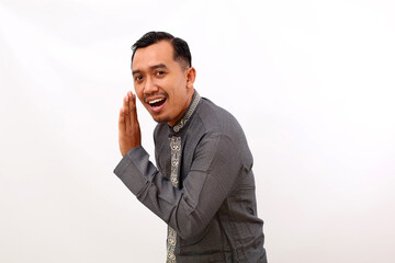 Happy asian man standing with telling secret hand gesture. Isolated on white background