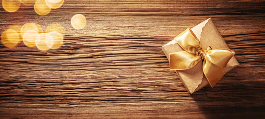 Kraft paper gift box with gold ribbon bow on old wood texture