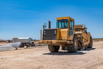 Obraz premium Yellow tractor, road repair. Side view. Watering machine in the background.