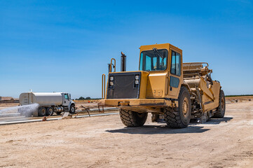 Side view of a large yellow tractor. The watering machine waters the road. Construction of the highway.