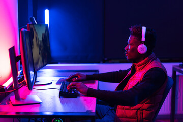 Young African man playing video game on computer. Streamer guy sitting at home and plays another match.