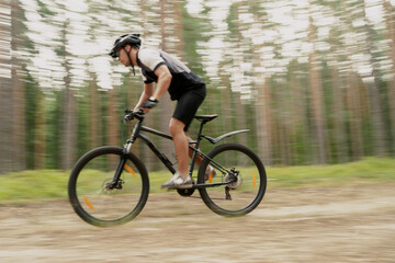 Fototapeta premium The photo in motion is blurry. A male cyclist riding a bicycle with a helmet, using a GPS activity tracker watch while training on a bicycle.