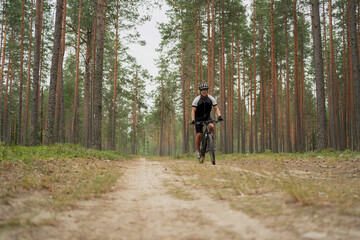 Obraz premium A male cyclist in the woods riding a bicycle with a helmet, using a GPS activity tracker watch while training on a bicycle.