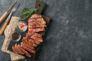 Steaks. Sliced grilled meat steak New York or Ribeye with spices rosemary and pepper on black marble board on old wooden background. Top view. Mock up.