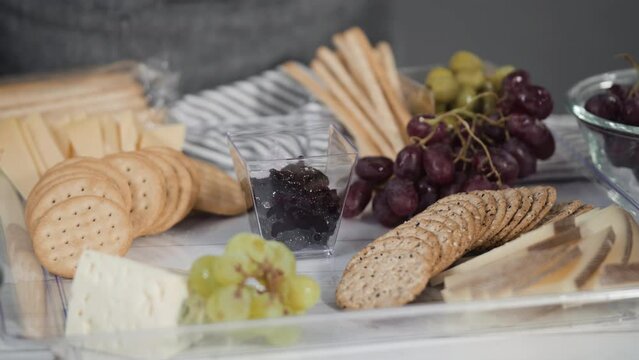 Step by step. Arranging cheese platter with fresh fruits, gourmet cheese, and crackers.