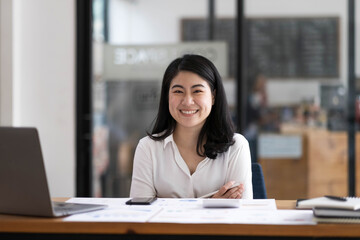 Charming Asian businesswoman sitting in the office with a digital laptop computer. Excited Asian businesswoman raising hands to congratulate while working in a modern office,