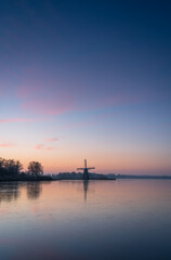 Fototapeta na wymiar Colourful dawn over a frozen lake with a windmill.