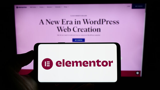 Stuttgart, Germany - 12-30-2022: Person holding cellphone with logo of Israeli software company Elementor Ltd. on screen in front of business webpage. Focus on phone display.