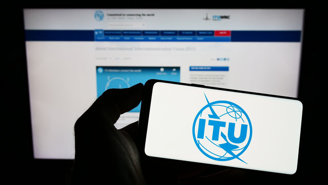 Stuttgart, Germany - 12-30-2022: Person holding mobile phone with logo of International Telecommunication Union (ITU) on screen in front of web page. Focus on phone display.