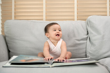 Baby girl reading a book  sitting on sofa at home