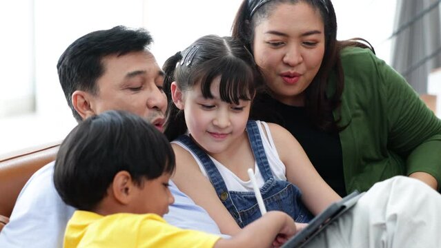 Asian father and mother looking children drawing a picture on teblet computer at home.