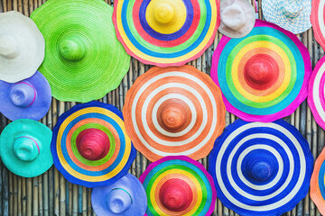 A variety of fashionable and colorful hats hanging on the bamboo backdrop of curbside shop. Women's designer hats from the sun of different colors. Design of women's beach hats. Beach hats for summer.