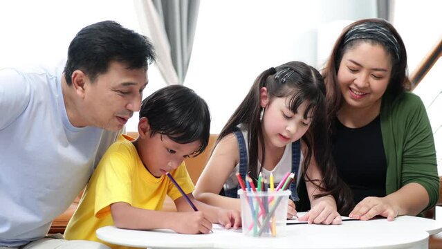 Asian father and mother looking children drawing a picture at home.