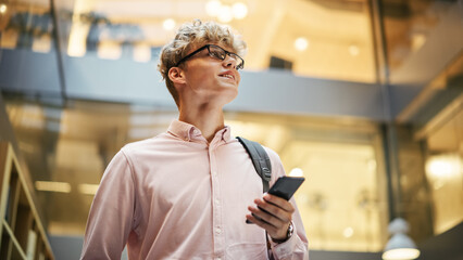 Portrait of Young Caucasian Man Feeling Confident as He Walks Smiling and Checking His Phone, in a...