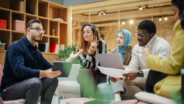 Group of Young Multiethnic People Working Together Using Laptop, Tablet and Charts in a Meeting Room. Energetic Teammates in a Meeting Room in an Office, Analyzing Statistics and Reviewing Data - Powered by Adobe