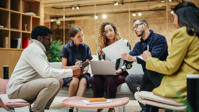 Multi Ethnic Group Of People Working On Developing Growth Ideas Based On Data. Energetic Teammates In A Meeting Room In An Office, Analyzing Charts Using Tablet And Laptop. Wide Shot