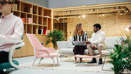Portrait of Two Creative Colleagues Collaborating and Pointing at the Laptop Screen in Office Hub. Hispanic Young Woman Discussing Work with Black Male Assistant
