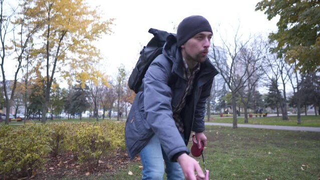 In search of lost domestic husky dog in city, adult Caucasian man calls puppy, attracting attention with treat for animals in city park in autumn cloudy weather. Responsible attitude to animals.