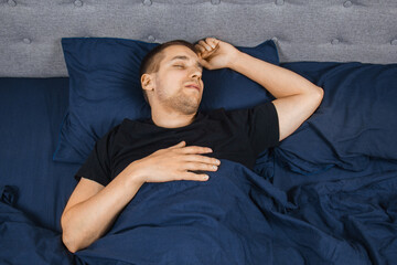 Top view of a handsome young man sleeping comfortably on the bed in his bedroom at night. Bachelor bedroom. Deep sleep.