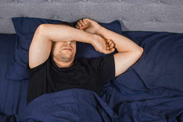 Top view of a handsome young man sleeping comfortably on the bed in his bedroom at night. Bachelor...
