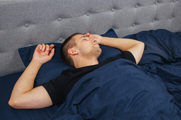 Top view of a handsome young man sleeping comfortably on the bed at night in his bedroom. Sleep in different positions. Bachelor bedroom. Deep sleep.