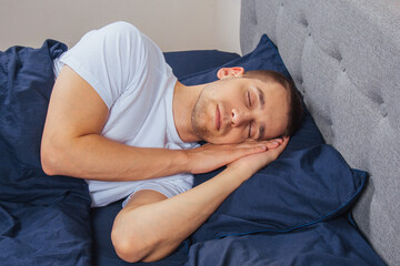 Top view of a handsome young man sleeping comfortably on the bed at night in his bedroom. Sleep in...