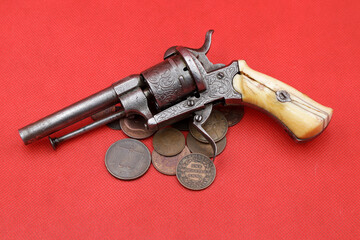 Vintage revolver and old coins of India on red background
