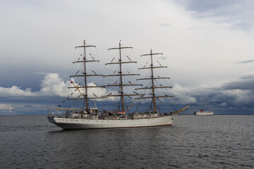 Three-masted sailing frigate goes to sea from the port against a stormy sky.