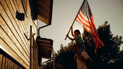Cinematic Shot of a Father Holding His Small Daughter of His Shoulders, Helping Her to Raise the United States of America Flag to Celebrate a National Fourth of July Holiday at Their House. - Powered by Adobe