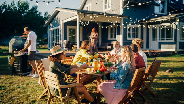 Big Family and Friends Celebrating Outside in a Backyard at Home. Diverse Group of Children, Adults and Old People Gathered at a Table, Kids Running and Having Fun.
