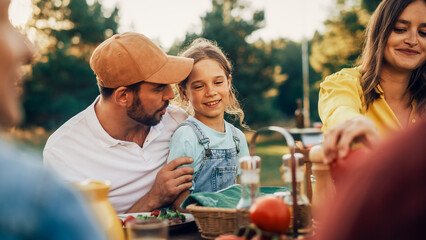 Portrait of a Handsome Young Father Holding His Cute Little Daughter on Lap at a Outdoors Dinner Party with Food and Drinks. Happy Family Having a Picnic Together with Friends.