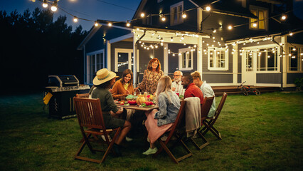 Parents, Children and Friends Gathered at a Barbecue Dinner Table Outside a Beautiful Home with...