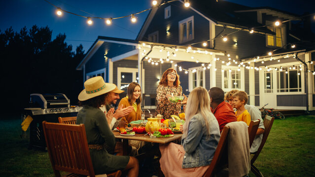 Group Of Multiethnic Diverse People Having Fun, Communicating With Each Other And Eating At Outdoors Dinner. Family And Friends Gathered Outside Their Home On A Warm Summer Evening.