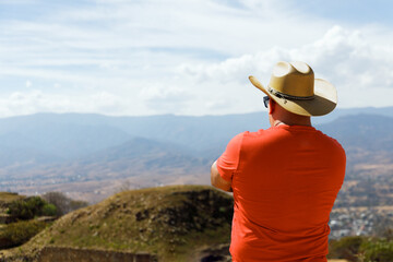 Latin American male wearing a cowboy hat while looking at the landscape. Man looking at Monte Alban ruins in Oaxaca Mexico