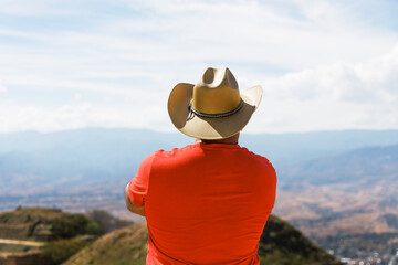 Latin American male wearing a cowboy hat while looking at the landscape. Man looking at Monte Alban ruins in Oaxaca Mexico