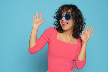 Young exotic happy brunette woman in pink blouse posing with a sunglasses on a blue studio...