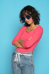 Young exotic brunette woman in pink blouse and rope belt jeans posing with a sunglasses on a blue studio background