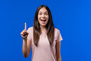 Happy teen girl having idea eureka moment, pointing finger up on blue background. Smart student...