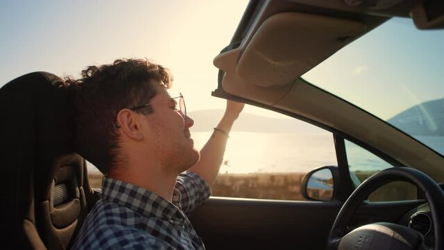 Young stylish man in sunglasses driving cabriolet car singing and dancing at golden sunset. Concept of success, tourism and rental. Happy smiling male tourist travel in California. Summer vacation