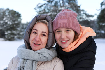 Concept of happy family, old age, emotions, walk in the winter forest of mom and adult daughter hugging outside. Woman smile. Around the green pine forest background of Christmas tree in forest.