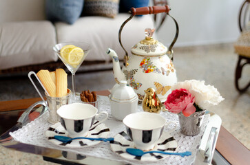 Teatime. Silver tray covered with lace with black and white stripes porcelain tea set, including teacups, plates, spoons, and sugar bowl, with sliced lime, cinnamon, and cookies