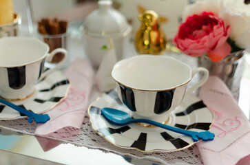 Black and white stripes porcelain tea sets, including tea cups, plates, spoons, napkin and sugar bowl on a silver tray covered with lace, decorated with tulips, a golden bird and cinnamon