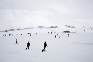 Skiers go downhill skiing on snow-covered mountain ski slope against the backdrop of a cloudy sky...