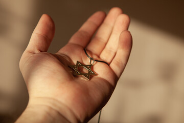 Closeup of pendant in the shape of the star of david on the hand of a man. Holocaust remembrance day.