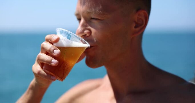 Man drinks beer on beach from plastic cup