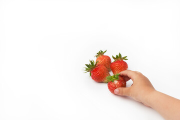 A child's hand reaches for ripe strawberries. The background is white. Copy space.