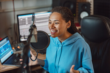 Young African anchorwoman, presenter talking into microphone at radio station. Entertainment and...