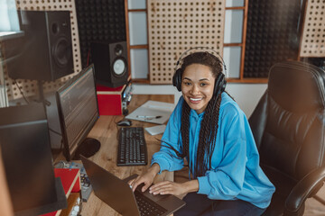 Beautiful woman sound engineer, radio presenter, smiles at camera while working on laptop in...