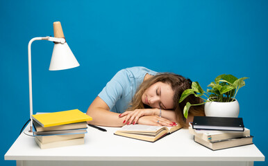 Tired student sleeping at her desk with books while having a lot of work. Busy schedule in college, workplace, sleep deprivation concept.