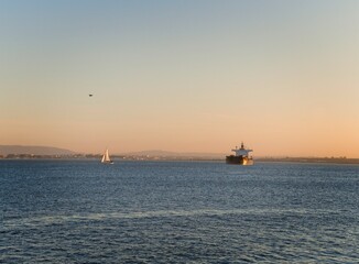Fototapeta premium Ship and sailboat on the Tagus River at sunset in Lisbon, Portugal